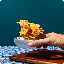 Hand holding a bowl of crispy fried food against a teal background