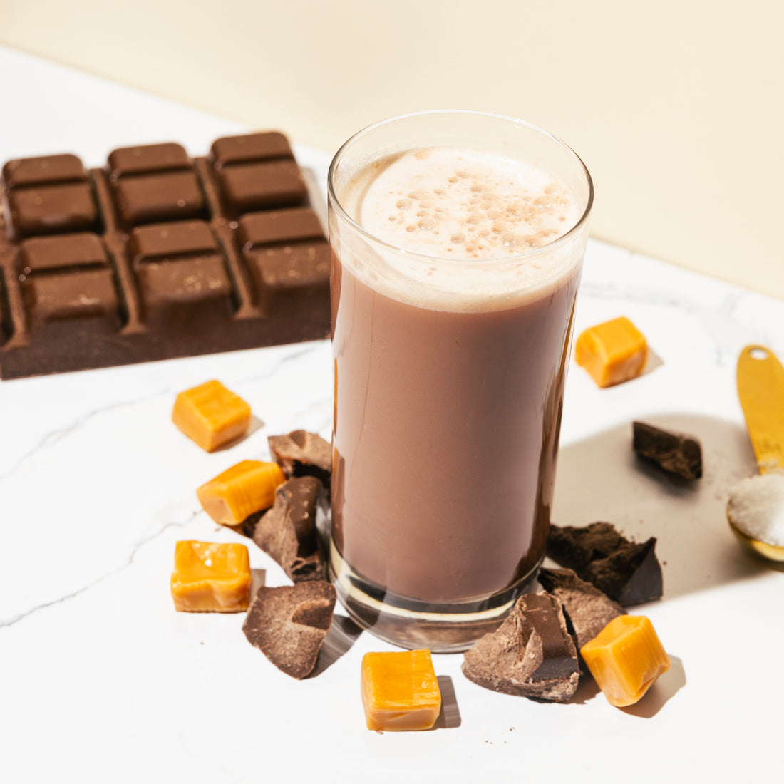 Glass of hot chocolate with chocolate bars and caramels on a white surface